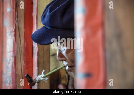 La province du Guizhou, Chine - CIRCA DÉCEMBRE 2018 : Une ancienne minorité ethnique homme se tenait dans l'embrasure de la porte et tira loin à sa pipe. Banque D'Images