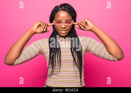 Young African American female essaie d'ignorer certains bruit gênant, bouchons oreilles avec les doigts, ferme un œil et soulève de sourcil, vêtus de outfi occasionnels Banque D'Images