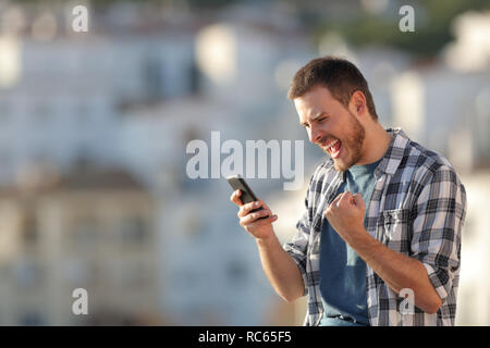 L'homme excité téléphone intelligent contrôle contenu dans une ville au coucher du soleil Banque D'Images