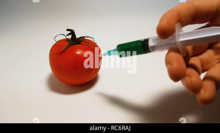 Part injecte une seringue d'un liquide vert ogm dans une tomate sur un fond blanc Banque D'Images