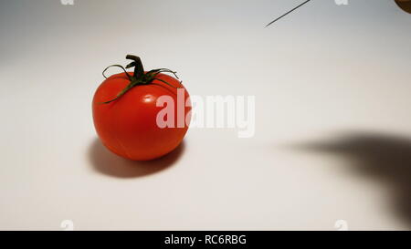 Part injecte une seringue d'un liquide vert ogm dans une tomate sur un fond blanc Banque D'Images