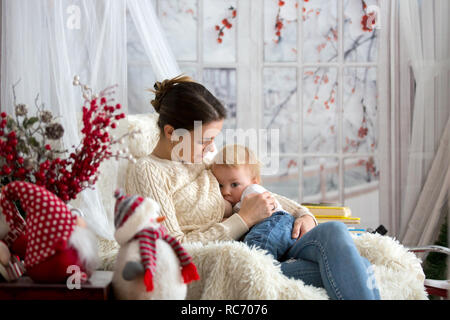 Mère d'allaiter son petit garçon assis dans un fauteuil confortable, en dehors de l'hiver neige Banque D'Images