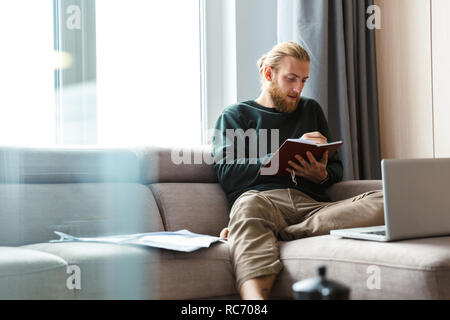 Image d'une jeune homme barbu assis dans Home la rédaction de notes. Banque D'Images