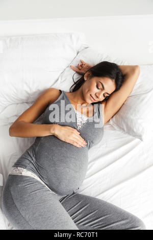 Image d'une femme enceinte en bonne santé à l'intérieur à la maison se trouve dans le lit. Banque D'Images