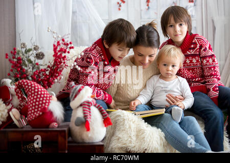 Mère lit livre à ses fils, des enfants assis dans un fauteuil confortable sur un jour d'hiver enneigé en hiver, Banque D'Images