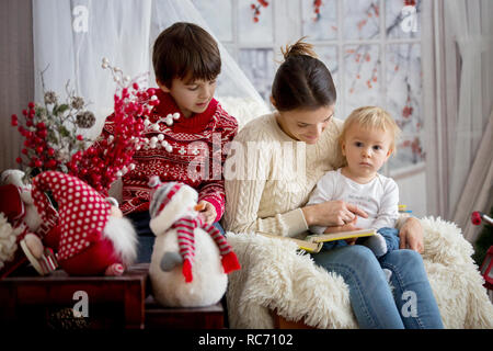 Mère lit livre à ses fils, des enfants assis dans un fauteuil confortable sur un jour d'hiver enneigé en hiver, Banque D'Images