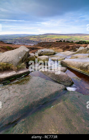 Rural pittoresque vue ensoleillée sur les collines et ville nichée dans la vallée, à partir de la Wharfe éperon rocheux & stream, en haut d'Ilkley Moor - West Yorkshire, Angleterre, Royaume-Uni. Banque D'Images
