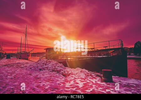 Scenic rouge violet et violet coucher de soleil sur la rivière campagne en Europe avec de vieux navires ayant reste à l'harfang harbour pier Banque D'Images