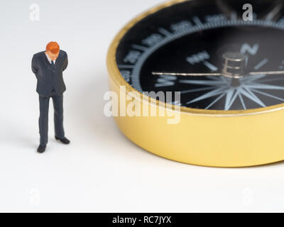 Figure miniature businessman en costume bleu foncé debout sur le côté de Golden Compass. Concept pour trouver la façon la façon de réussite des entreprises Banque D'Images