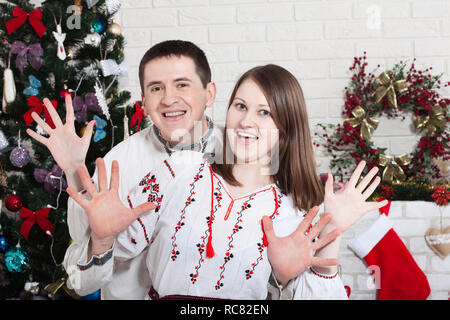 Cheerful couple holding hands bénéficiant ensemble la veille de Noël. Le temps de Noël à la maison. Une authentique jeune couple en ukrainien shirts. Banque D'Images