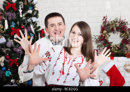 Cheerful couple holding hands bénéficiant ensemble la veille de Noël. Le temps de Noël à la maison. Une authentique jeune couple en ukrainien shirts. Banque D'Images