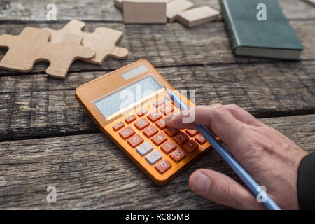 Part d'un étudiant ou d'un comptable à l'aide de la calculatrice sur son bureau en bois avec des pièces de puzzle et de patères et vert notes sur la 24. Banque D'Images