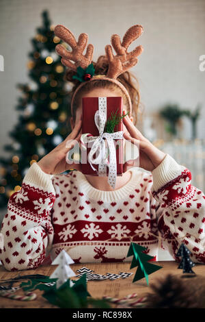 Femme derrière cadeau de Noël, Décorations de Noël en forme d'arbre en premier plan Banque D'Images