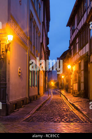 Une rue étroite le long de la cité médiévale maisons à colombages de la vieille ville de Quedlinburg éclairée par la chaude lumière des lampes dans la soirée Banque D'Images