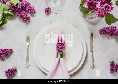 Table élégante place au printemps avec des fleurs de lilas, de l'argenterie sur fond clair. Vue d'en haut. Banque D'Images