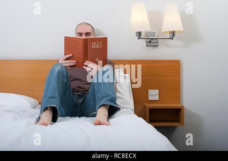 Homme, 30-40 ans, la lecture de la Sainte Bible dans une chambre d'hôtel Banque D'Images