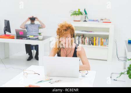 Businesswoman typing on laptop at office desk lors de l'écoute au casque