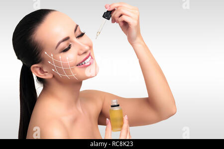 Photo de Gros plan sur l'application de l'huile cosmétique young woman's face à la pipette. Concept de soins de beauté. Fond d'acier gris Banque D'Images