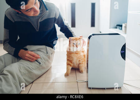 Déshumidificateur avec l'écran tactile, l'indicateur d'humidité, uv lampe, air ioniseur, récipient de l'eau travaille à la maison tandis que l'homme de caresser son chat. Sécheur d'air Banque D'Images