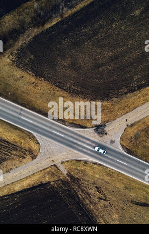 Vue aérienne de la voiture blanche unique de la conduite sur route à travers la campagne ordinaire dans l'après-midi d'hiver froid sans neige Banque D'Images