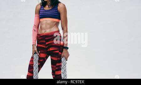 Athletic femme debout tenant deux cordes de bataille lors de l'entraînement. Cropped shot d'une femme en travail d'usure de remise en forme à l'aide de bataille des cordes. Banque D'Images