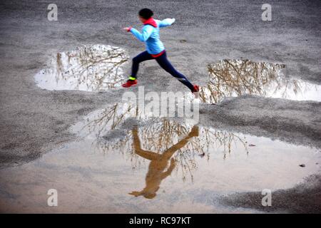 Young woman jogging en hiver, sautant par dessus les flaques de pluie imperméable et coupe-vent, vêtu de vêtements de performance Banque D'Images