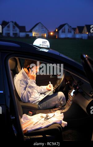 Jeune médecin, omnipraticien travaillant dans le pays, faisant appel téléphonique et prise de notes dans sa voiture après une soirée home Banque D'Images