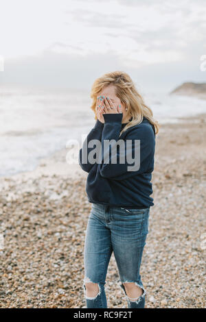 Jeune femme couvrant son visage avec les mains de plage, Menemsha, Martha's Vineyard, Massachusetts, USA Banque D'Images