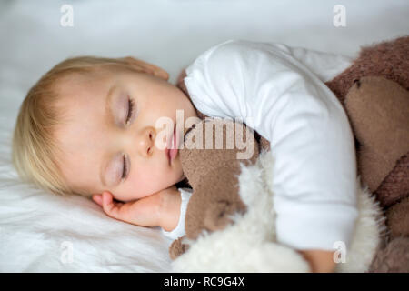 Sweet baby boy in mignon dans l'ensemble, de dormir dans le lit avec ours en peluche peluches, paysage d'hiver derrière lui Banque D'Images