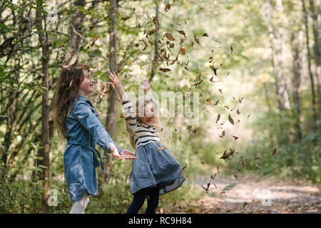 Soeurs de jeter les feuilles en forêt dans l'air Banque D'Images