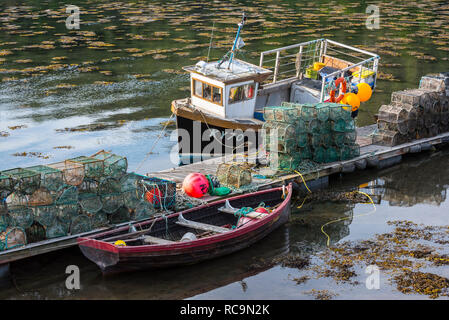 Petit bateau de pêche amarrés et des casiers à homard / prawn nasse empilés sur la jetée dans le port de Plockton, Highlands, Scotland, UK Banque D'Images