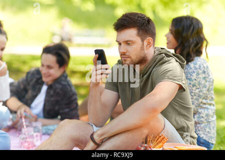 Man using smartphone à pique-nique avec des amis Banque D'Images