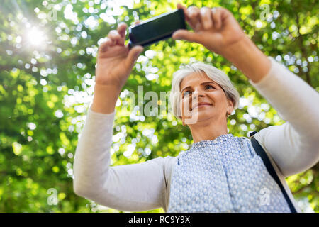 Senior woman photographing par cellule au parc d'été Banque D'Images