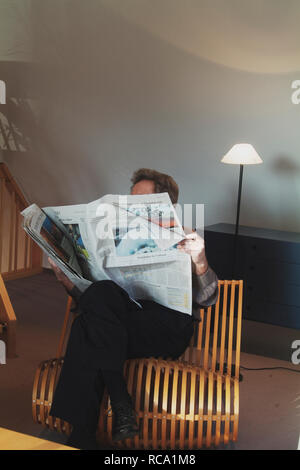 Mann mittleren modifie liest Zeitung auf einem Stuhl | homme d'âge moyen est de lire le journal sur une chaise Banque D'Images