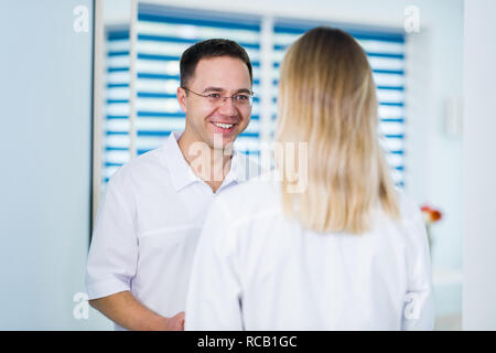 Beau jeune médecin parle avec sa belle assistante, debout dans salle d'attente du centre Banque D'Images