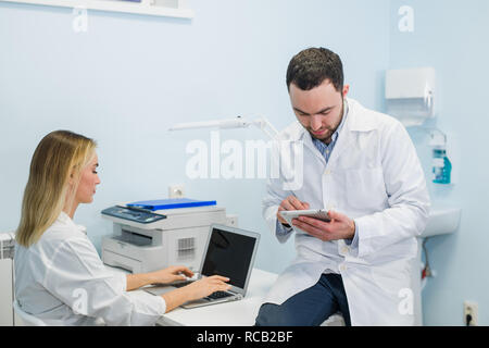 Deux collègues médecins sont assis dans les lieux de travail et de l'utilisation de la technologie moderne pour leur travail, en blouse blanche, l'accent Banque D'Images