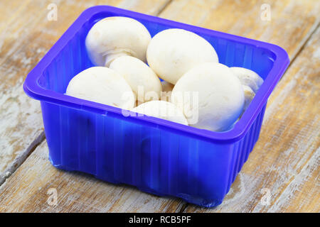 Champignons frais dans la boîte bleue en plastique sur la surface en bois Banque D'Images