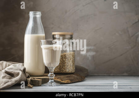 Le lait d'avoine non dairy pour alimentation végétalienne. Flocons d'avoine dans un bocal en verre et verre bouteille de lait sur fond rustique. Copie de l'espace pour votre texte Banque D'Images
