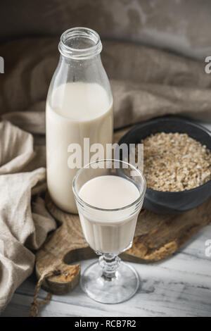 Le lait d'avoine non dairy pour alimentation végétalienne. Flocons d'avoine dans un bol de verre et bouteille de lait sur fond rustique Banque D'Images