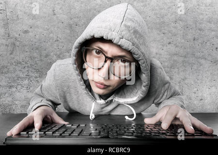 Un hacker (programmeur) dans une hotte et verres contre un mur de béton ressemble étrangement à l'appareil photo Banque D'Images