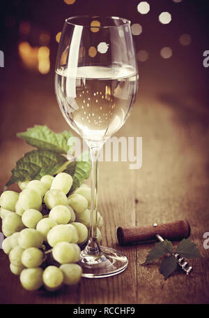 Verre de vin blanc élégant avec des tas de raisins verts frais et ouvre-bouteille sur une table en bois avec un bokeh de lumières parti mousseux Banque D'Images