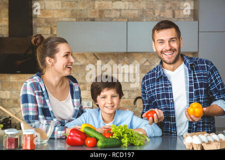 Mère Père et fils à la maison debout dans la cuisine ensemble à rire caméra man holding ludique pour poivrons juggling Banque D'Images