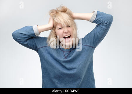 Choqué la panique girl pull bleu en tenant les mains sur la tête et hurlant de désespoir et de frustration tout en étant en retard au travail. Des yeux plein de terr Banque D'Images