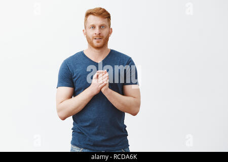 L'homme se frotter les mains, se sentant venir beaucoup. Portrait d'excité et intrigué de businessman with ginger hair et toucher soie poitrine près de palms et souriant avec expression curieux Banque D'Images