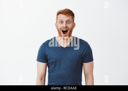 Wow, incroyable. Portrait de charmé et enchanté beau heureux redhead copain avec soies, de laisser tomber la mâchoire et tout sourire, regardant avec expression excité à quelque chose d'impressionnant et passionnant Banque D'Images