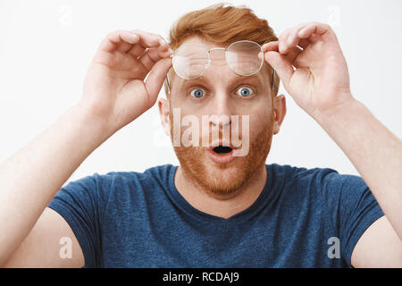 Portrait de choqué et impressionné accablé redhead guy avec barbe, enlever les verres et holding jante sur le front, les lèvres de pliage et a fixer avec des yeux à sauté impressionnant et curieux Banque D'Images