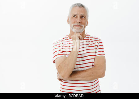 Portrait de senior charmant heureux et satisfaits à grand-père après avoir regarder le jardin de rêve dans le coin en haut à gauche sur la main tenant le menton debout dans une pose smiling ravis Banque D'Images