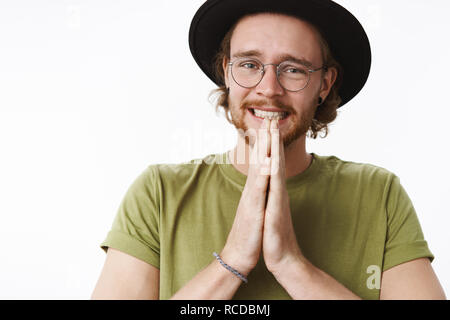 Close-up shot de beau mâle nerveux coworker avec barbe et Nez Percé dans les verres, le serrement des dents veuillez dire chapeau sourcils de levage dans l'espoir que la tenue des mains dans la prière et la mendicité pour aider Banque D'Images