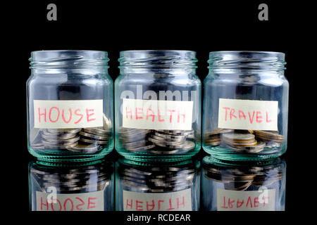 Les bocaux en verre avec des pièces de monnaie et sur fond noir : maison,santé, voyage, Banque D'Images