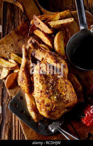 Grillades de Poisson ou de poulet assaisonné de printemps frits servis avec les quartiers de pommes de terre et tomates sur une vieille planche de bois (vue de dessus Banque D'Images